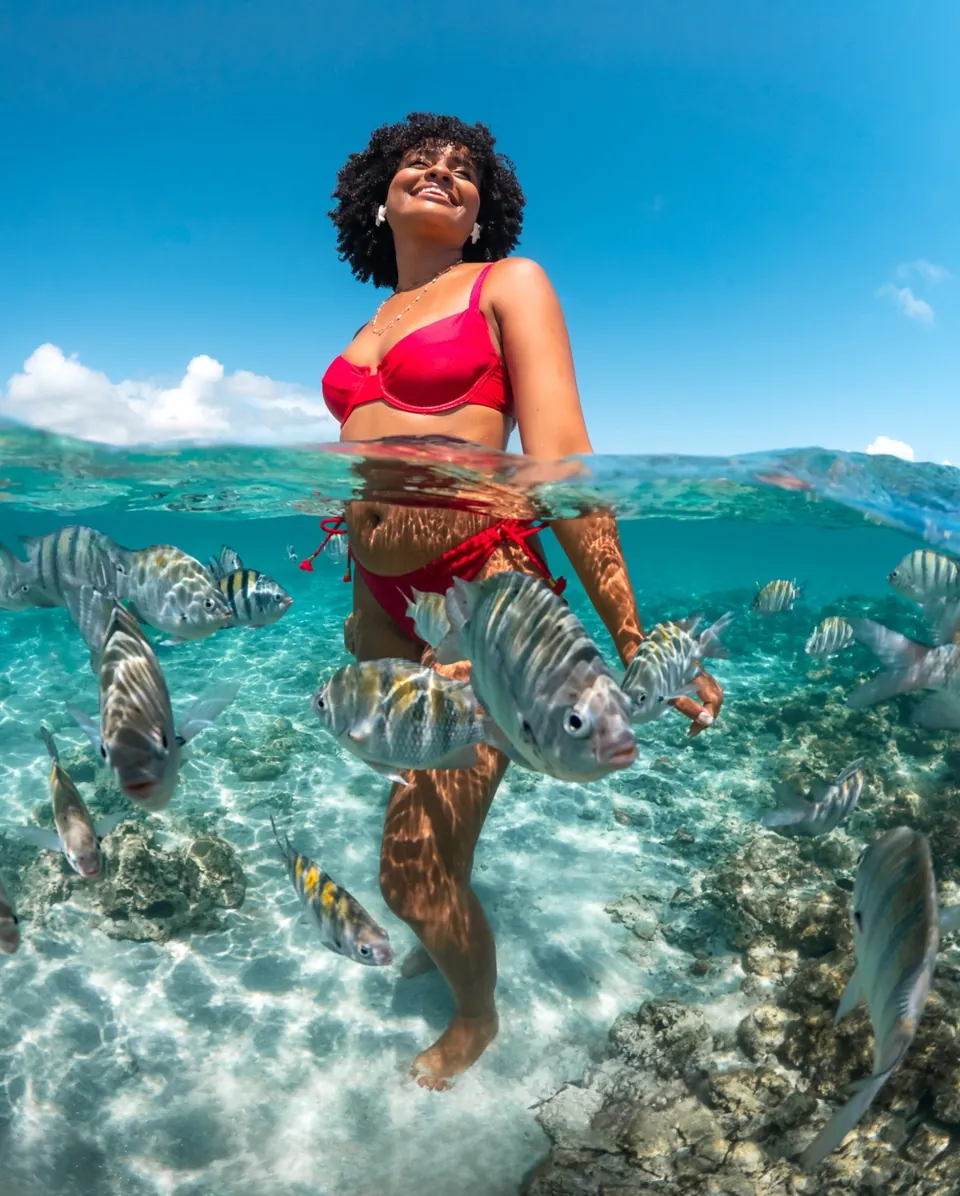 Mulher de biquíni vermelho em foto meio dentro, meio fora d'água nas piscinas naturais